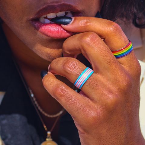 girl with long black nails wearing a rainbow gay pride ring on her index finger and a transgender pride ring on her ring finger