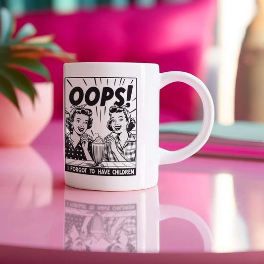 Small white mug sitting on pink table with the word Oops I forgot to have children in bold with 1950s style women smiling and drinking a milkshake