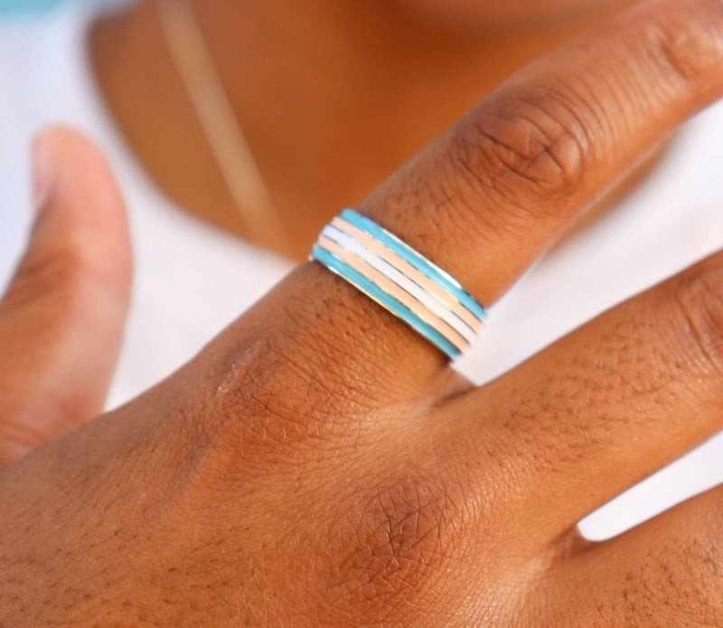 brown skinned model wearing trans pride ring holding hand up to camera