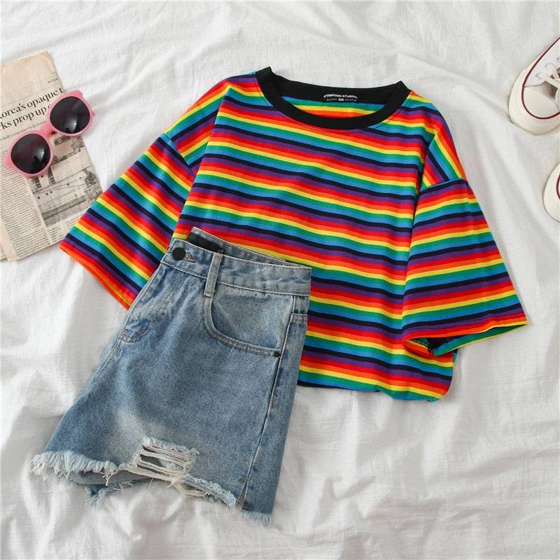 Folded Shirt with striped colors laying next to a pair of blue jean shorts and sunglasses